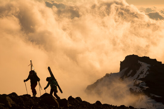 Two skiers hike up a steep rocky mountain during sunset La Parva, Chile