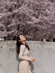 Outdoor portrait of beautiful young Chinese girl posing eyes closed with blossom cherry flowers background in spring garden, beauty, summer, emotion, lifestyle, expression and people concept.