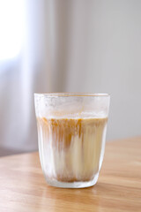 Dirty coffee in transparent glass on wooden table with bright and blur background