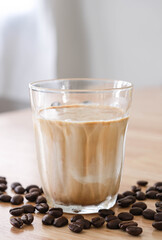 Dirty coffee in transparent glass on wooden table There are coffee beans lying around the mug with blur background