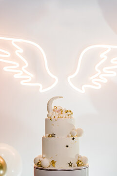 Trendy cake with decor. Celebration baptism concept. Arch decorated balloons, angel wings. Reception at birthday baby party on wall. Delicious reception on photo zone, area. Closeup.