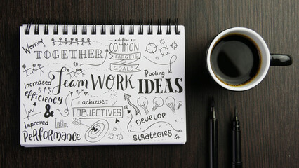 TEAMWORK graphic notes in notebook with cup of coffee and pens on black wooden desk