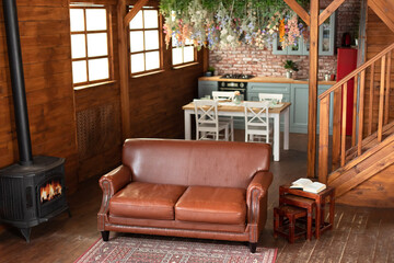 Stylish studio apartment interior with comfortable brown sofa and cast iron wood stove. Trendy...