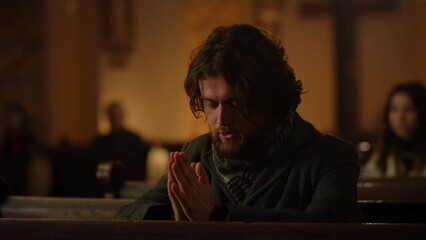 A brunette man folds his arms and prays. Close-up of a man in a catholic church praying during the Sunday service.
