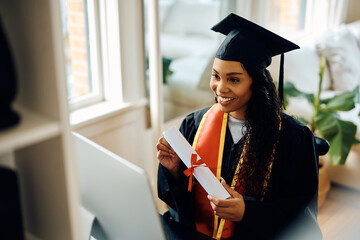 Happy black student showing her graduation diploma during video call. - obrazy, fototapety, plakaty