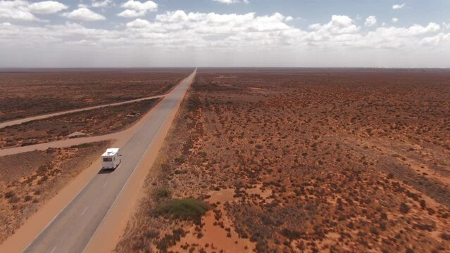 Campervan driving on an empty long straight road in a barren environment in South Australia. Drone follow shot