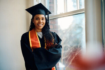 Happy black graduate student standing with her arms crossed and looking at camera.