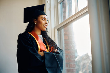 Confident African American graduate student standing with her arms crossed by window.