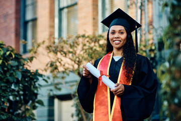 Happy African American female student holding her diploma on graduation day and looking at camera.
