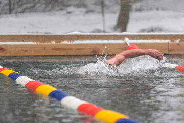 A man swimming in a lake at an ice swimming competition while snow is falling