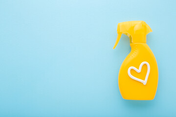 Heart shape created from white cream on yellow spray bottle of sunscreen. Light blue table background. Pastel color. Care about body skin protection in summer. Empty place for text. Top down view.