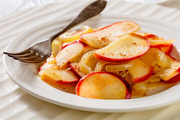 fried onion and red apple slices on white plate with fork on white wood table, landscape view from above, close-up