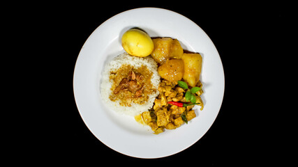 High Angle of Chicken curry rice in yellow spice sauce with potatoes and boiled egg served on white plate isolated on black dark background. Top view angle Chicken curry rice.