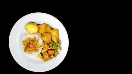 High Angle of Chicken curry rice in yellow spice sauce with potatoes and boiled egg served on white plate isolated on black dark background. Top view angle Chicken curry rice.