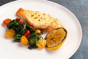 Salmon steak with cheese crust and salad with tomatoes in a plate.