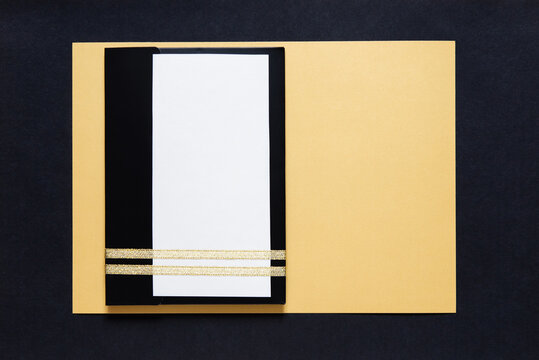 Black envelope mockup, Flat Lay, on gold background with copy space. Tied with gold ribbon. Envelope is a white blank card for text. Business invitation, congratulations on Mother's Day, Father's Day.