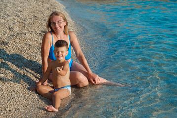 Happy  woman mother and little son  sitting on sea ocean beach at vacation resort  in Porec, Croatia