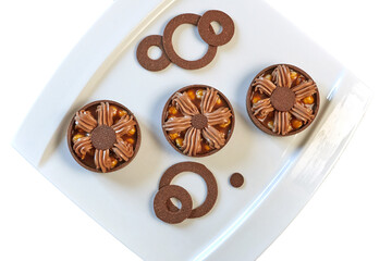 Sweet dessert: Tarts, Tartlets. Dark brown chocolate shortbread baskets filled with nuts, caramel, and coffee cream. Close-up on a white plate