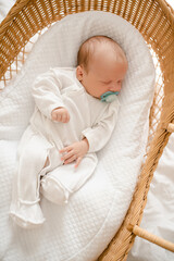 Cute baby sleeping in straw cradle wearing pajamas and with pacifier top view. Childhood.