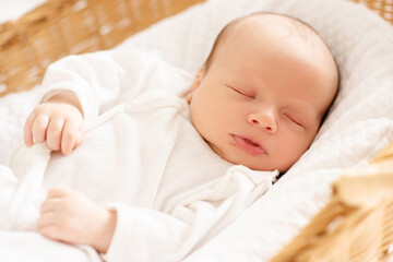 Little baby infant 1-2 months old sleeping in straw crib with closed eyes wearing white pajamas at...