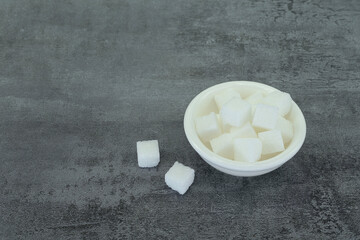 Sugar cubes in bowl on stone texture background.