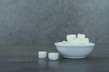Sugar cubes in bowl on stone texture background.
