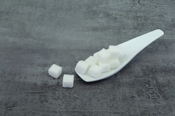 Sugar cubes in spoon on stone texture background.