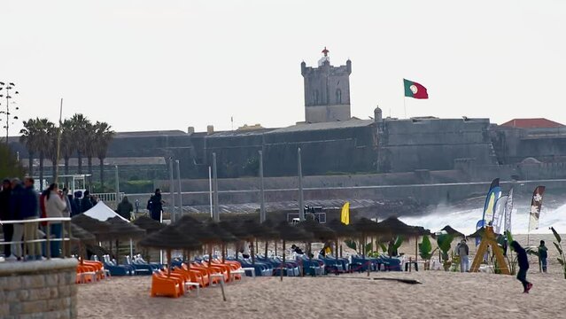 The photographers team and surfers waiting for the big event with perfect waves and the best tube riders in Carcavelos in a perfect chapter with fort Saint Julian and portuguese flag in background.