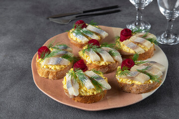 Homemade sandwiches with salted herring, cheese and egg, decorated with beetroot rose on plate on gray table