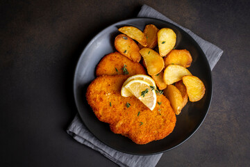 Chicken schnitzel with sauce, fried potatoes and lemon in a plate