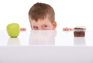 A young boy tempted by the sight of a chocolate cake and an apple on a table making an unhealthy decision, choosing sweets or unhealthy snacks such as a cupcake isolated on a PNG background.