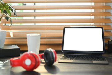 Comfortable workplace with digital tablet, potted plant, coffee cup and headphone on black wooden desk