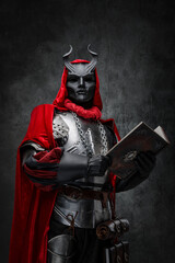 Shot of mysterious cultist dressed in steel armor and red mantle holding book.