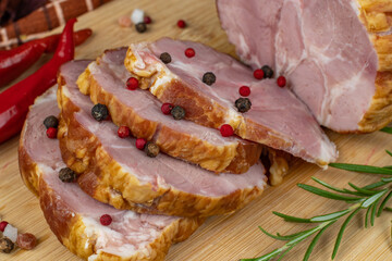 On a wooden cutting board, sliced juicy pork ham, carving knife, red hot peppers, multi-colored allspice, parsley, dill and basil. Panoramic close-up. The concept of delicious pork products
