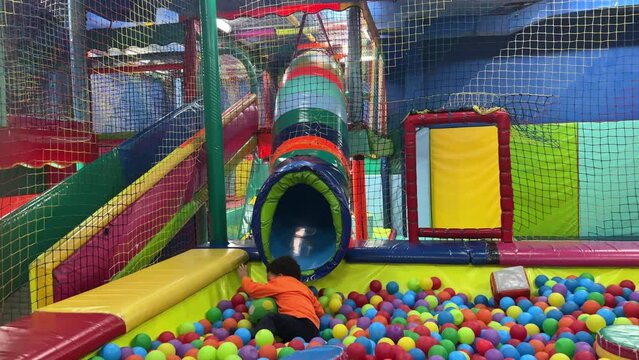 Exotic two-year-old black baby having fun in a children’s park. His face is painted and he wears an orange tracksuit. Color balls pool.