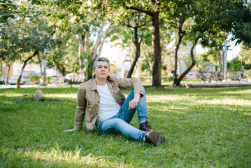 Fototapeta premium Portrait of gray haired man in a park with positive expression sitting on the grass looking at the camera.