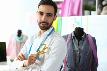 Smiling handsome fashion designer with scissors standing next to mannequin at workplace