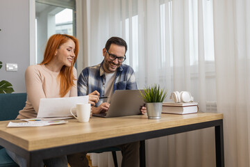 Young man and woman smiling while planning further work together and using laptop at home