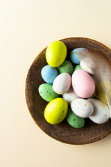 Multi colored eggs with natural feather on beige background for happy easter concept or greeting card