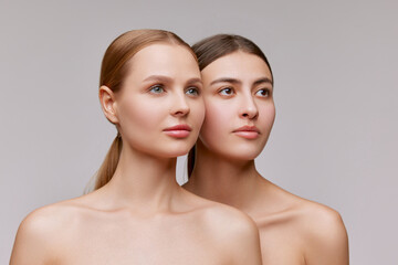 Couple of beautiful elegant young women, blond and brunette with well-kept skin posing over light...