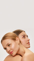 Vertical portrait of two adorable young girls with well-kept skin posing over grey background. Models with bare shoulders. Concept of beauty, spa, skin care and health