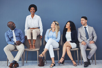 Black woman, chair and smile with business people for interview with comic laugh, lobby or wall...