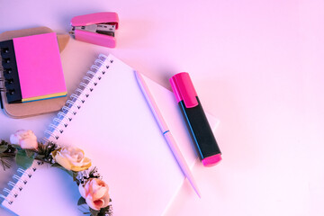 Material de oficina rosa con una corona de flores apoyada en una libreta sobre un fondo rosa por el día internacional de la mujer. - obrazy, fototapety, plakaty