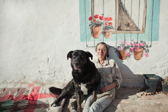 Mature woman sitting on the ground with her dog as they relax and sunbathe together