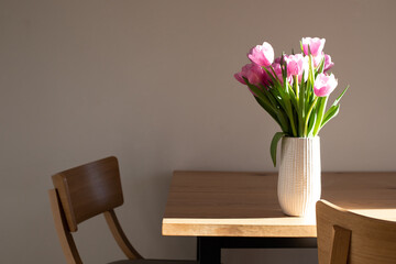 Gently pink bouquet of tulips in a white vase on wooden table. Spring background with a bouquet of flowers. Front view