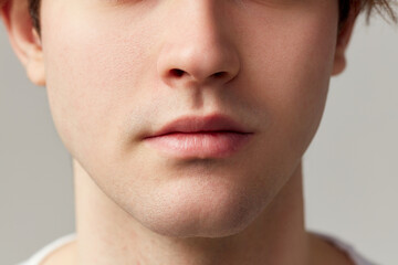 Cropped image of male face nose, lips, chin. Young model posing over grey studio background....