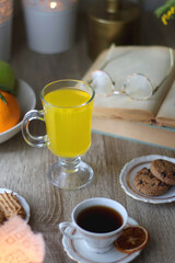 Cup of tea, plates with cookies, glass of orange juice, books, reading glasses, bowl of fruit and candles on the table. Selective focus.