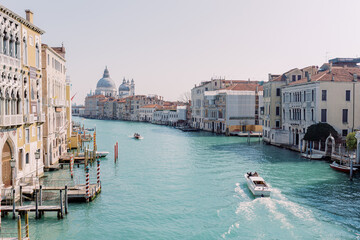 A motorboat cruises a river in Venice, with the city in the background. Sun, blue sky, turquoise...