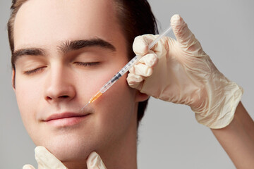 Lip augmentation. Close-up of young man doing beauty cosmetological injections. Male model against...