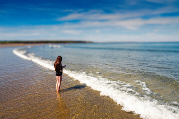 Teenager girl in dark t shirt in the ocean, Blue cloudy sky in the background. Summer time and holiday mood. Enjoy open fresh water and play with waves concept. Selective focus.